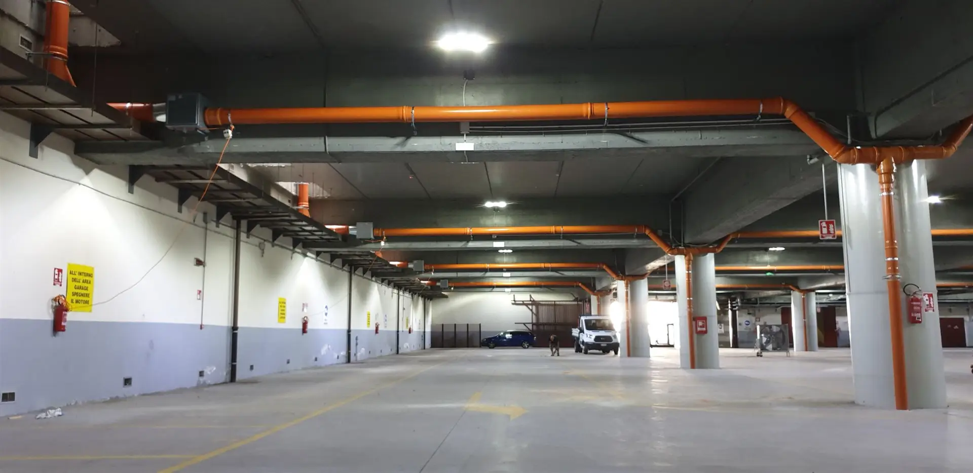 Autorimessa interrata con tubazioni arancioni lungo il soffitto e le colonne